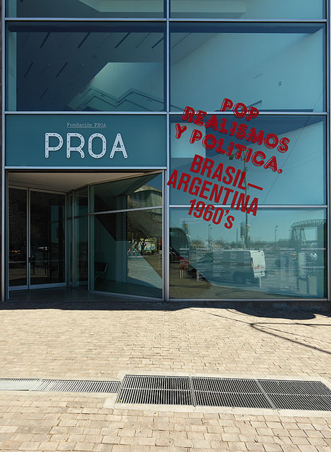 La marca Proa aplicada al vidrio, elemento central de la identidad arquitectónica, junto a gráfica de entorno de la exposición actual.